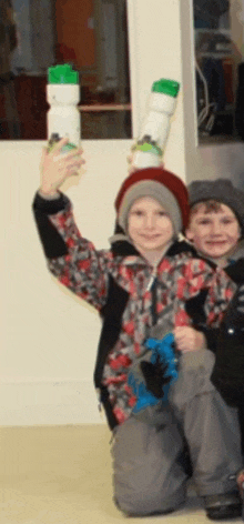 two young boys are sitting on the floor holding up their water bottles