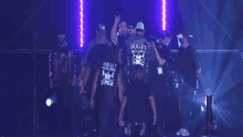 a group of men are standing in a dark room and one of them is wearing a shirt that says bullet club