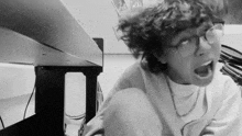 a black and white photo of a person with curly hair and glasses making a funny face