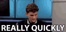 a young man in a black jacket is sitting in front of a sign that says `` really quickly '' .