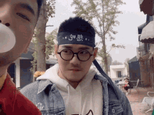 a man wearing glasses and a headband with chinese writing on it blowing bubble gum