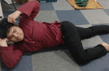 a man in a red shirt and black pants is laying on his stomach on the floor .