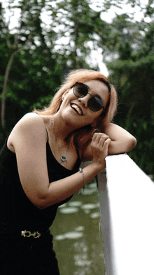 a woman wearing sunglasses leans on a railing and smiles