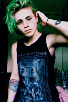 a girl with green hair is wearing a black tank top that says darkness we stand