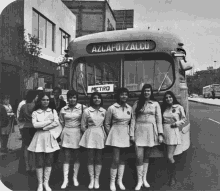 a group of women standing in front of a bus that says metro on the front