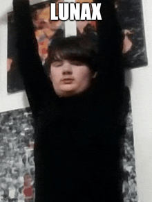 a young man is standing in front of a wall with his arms in the air and the name lunax written on it .