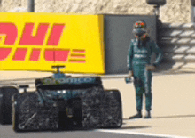 a man in a helmet stands next to a race car with dhl written on it