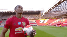 a man in a red jersey is walking on a soccer field holding a ball .