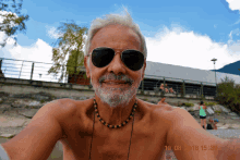 a shirtless man wearing sunglasses and a beaded necklace takes a selfie on 19.08.2013