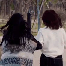 two women are standing next to each other on a sidewalk in a park with their hair blowing in the wind .