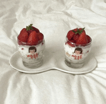 two glasses filled with strawberries and yogurt are on a plate