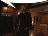 a man with a beard is dancing in a room with a refrigerator in the background