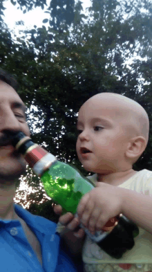 a man with a mustache is holding a baby who is drinking from a green bottle