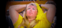 a woman wearing a yellow shirt and a yellow pom pom on her head is watching a game .