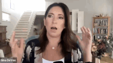 gina devee is talking on a video call in a living room with stairs in the background .