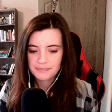 a woman wearing headphones and a plaid shirt is sitting in front of a microphone in front of a bookshelf .