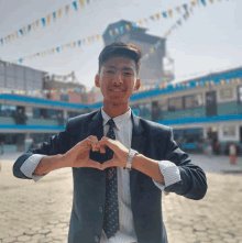 a man in a suit and tie makes a heart shape with his hands