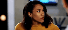 a woman wearing a yellow sweater and earrings is looking at the camera .