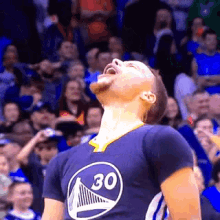 a basketball player wearing a golden state warriors jersey is standing in front of a crowd with his mouth open .