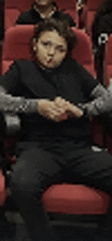 a young boy is sitting in a row of red chairs in a movie theater .