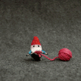 a crocheted gnome is knitting while holding a ball of red yarn