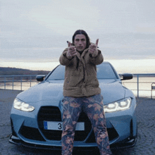 a man is standing in front of a blue car giving a thumbs up .