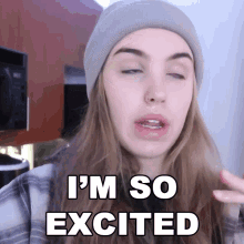 a woman wearing a beanie and a plaid shirt says " i 'm so excited "