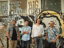 a group of men standing in front of a wall with graffiti that says do the right thing