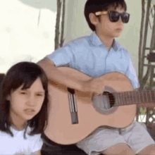 a young boy is playing a guitar next to a young girl .