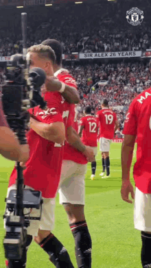 a group of soccer players are on a field with a sign that says sir alex 26 years in the background