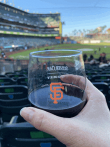 a person holding a glass with a sf logo on it in front of a baseball stadium