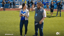 a man and a woman are standing on a baseball field and the man is wearing a la dodgers shirt