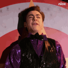 a man in a purple sequined shirt and black vest is standing in front of a nick logo