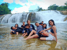 a group of people are posing for a picture in the water near a waterfall .