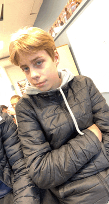 a young boy in a black jacket with his arms crossed looks at the camera