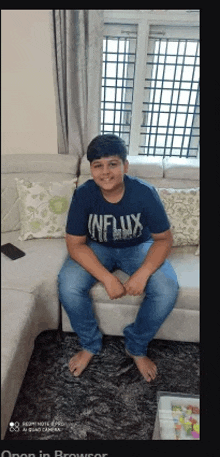 a young boy is sitting on a couch in a living room wearing a blue shirt and jeans .