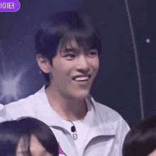 a young man in a white jacket is smiling in front of a crowd of people .