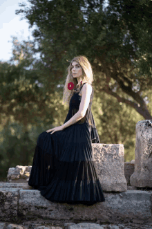 a woman in a black dress is sitting on a stone wall