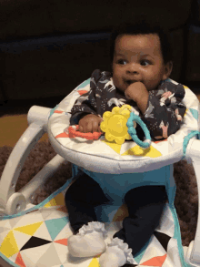 a baby is sitting in a bouncer with a toy in his mouth