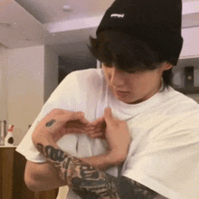 a person with a tattoo on their arm making a heart shape with their hands .