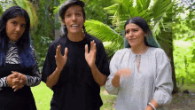 three women are standing next to each other in a park . one of the women has blue hair .