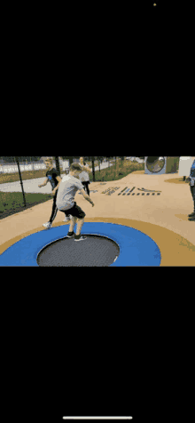 a boy is jumping on a trampoline in a park while other people watch .