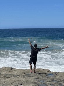 a man with his arms outstretched stands on a rocky cliff overlooking the ocean