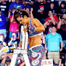 a woman in a colorful outfit is holding a trophy in front of a crowd with a sign that says urn