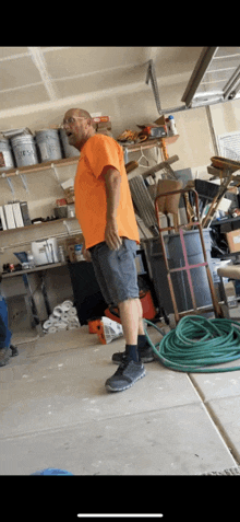 a man in an orange shirt is standing in a garage with a green hose