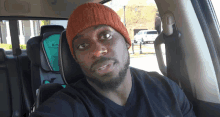 a man wearing an orange beanie sits in a car seat