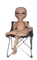 a statue of an alien is sitting on a folding chair