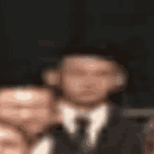 a blurry picture of a man in a suit and tie with a hat on .