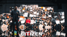 a man in a suit stands in front of a crowd of protesters with the word citizen on the bottom right