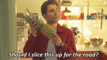 a man in a red jacket is holding a pineapple and saying should i slice this up for the road ?